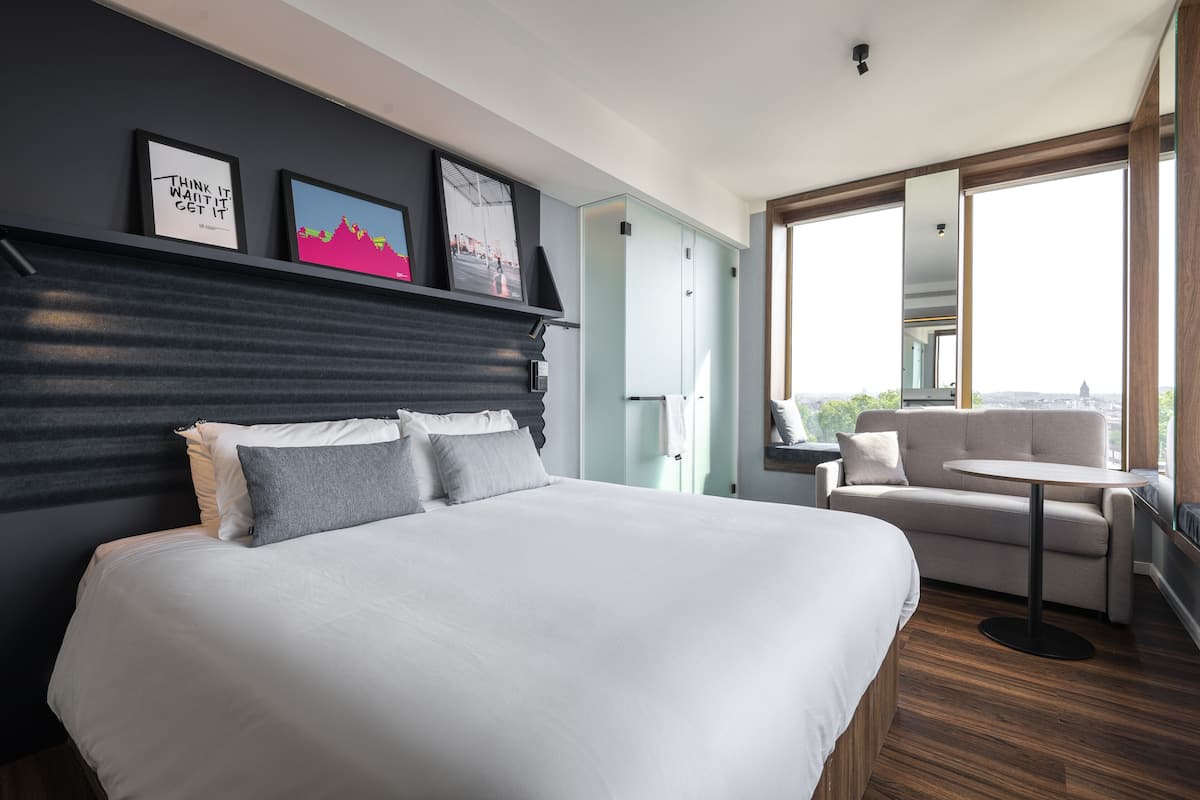 Une chambre d’hôtel moderne avec un grand lit, un canapé, une petite table et un balcon offrant une vue agréable.