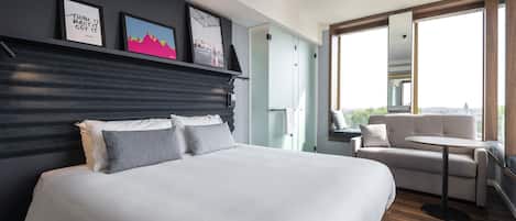 Una habitación de hotel moderna con una cama grande, un sofá, una mesita y un balcón con vistas.