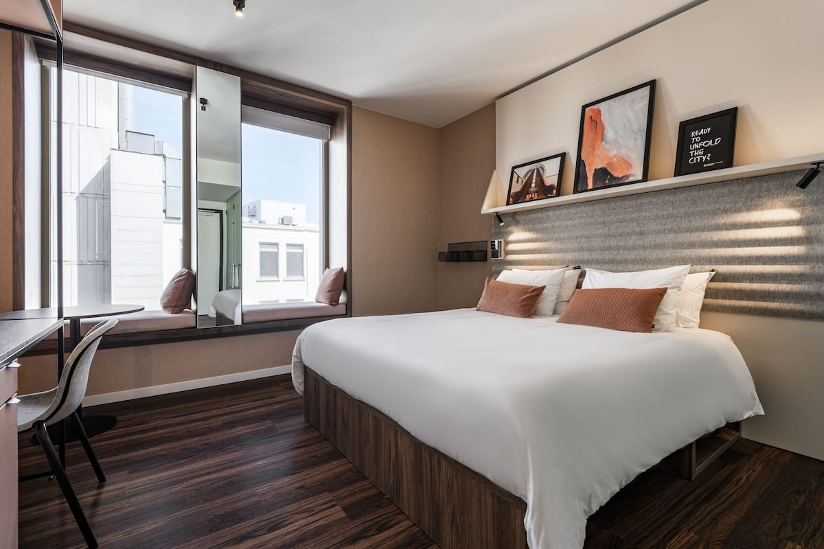 Une chambre d’hôtel moderne dotée d’un grand lit, d’un bureau et d’une fenêtre donnant sur la ville.