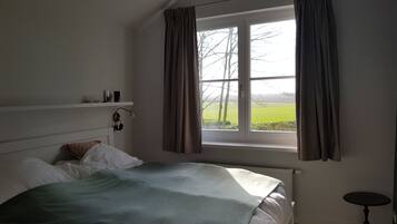 A bedroom with a bed, a window with curtains, a bedside table, and a shelf with items.