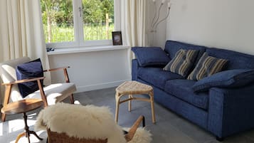A living room with a blue sofa, a wicker chair, a small table, and a large window with curtains.