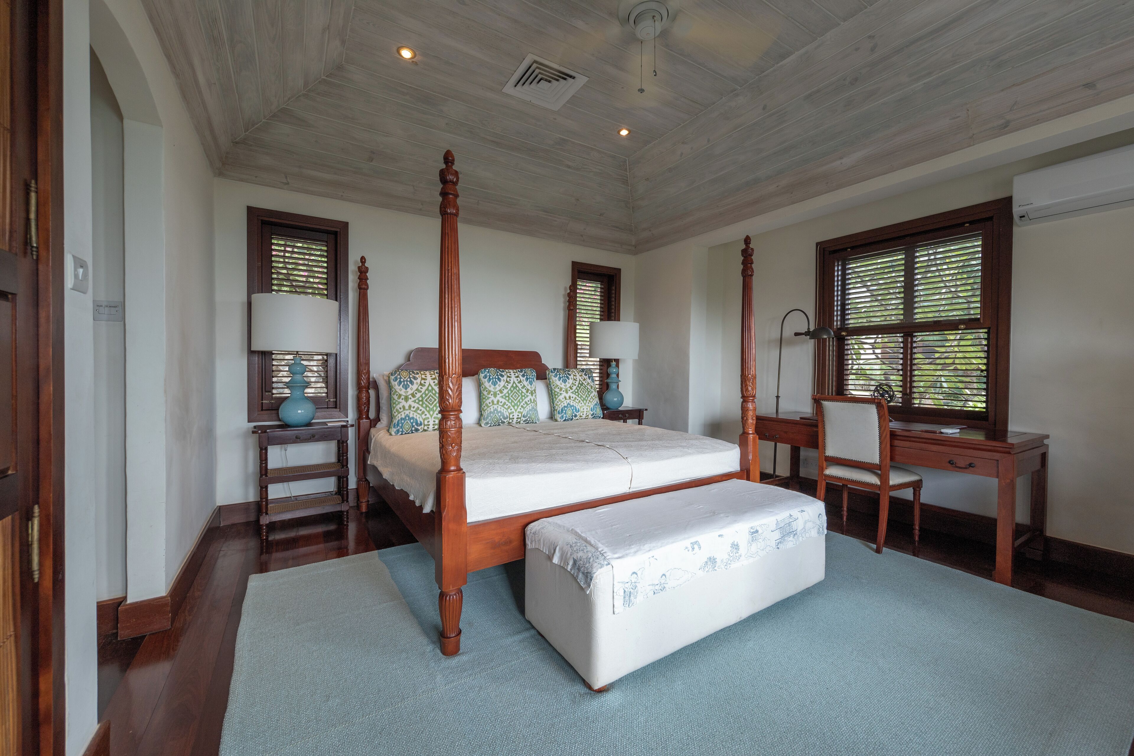 A four-poster bed with a matching bench, a desk, and two lamps.