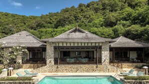 A three-story stone building with a swimming pool, outdoor seating, and a view of a forested hillside.