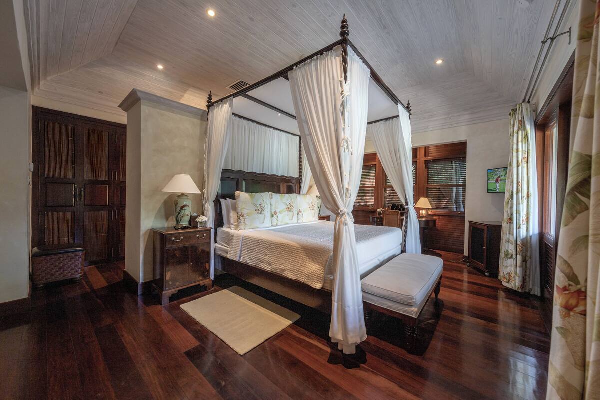 A four-poster canopy bed with a white canopy, a wooden headboard, and a bedside table with a lamp.