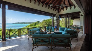 A covered outdoor seating area with wicker furniture and a view of the ocean.