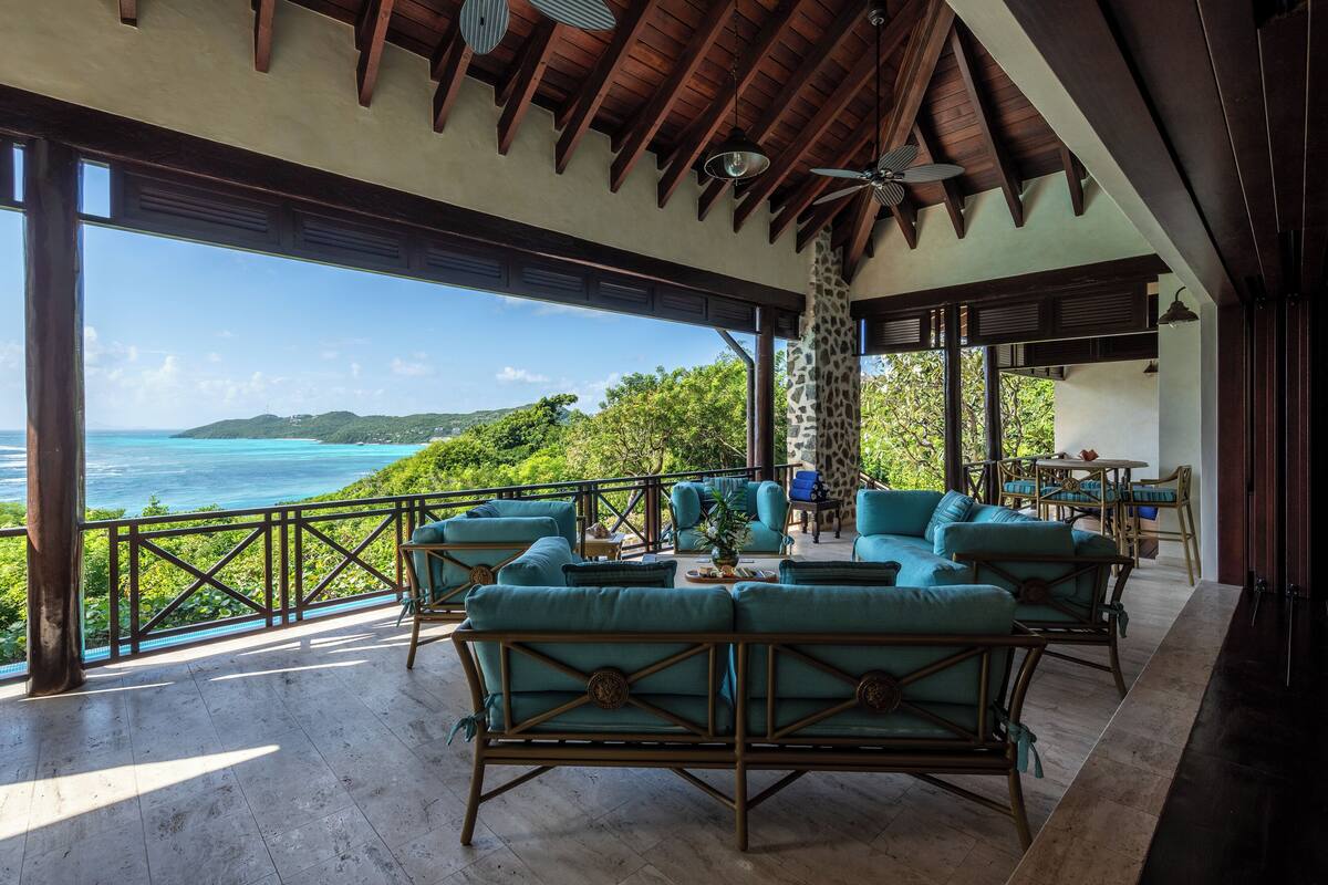 A covered outdoor seating area with wicker furniture and a view of the ocean.