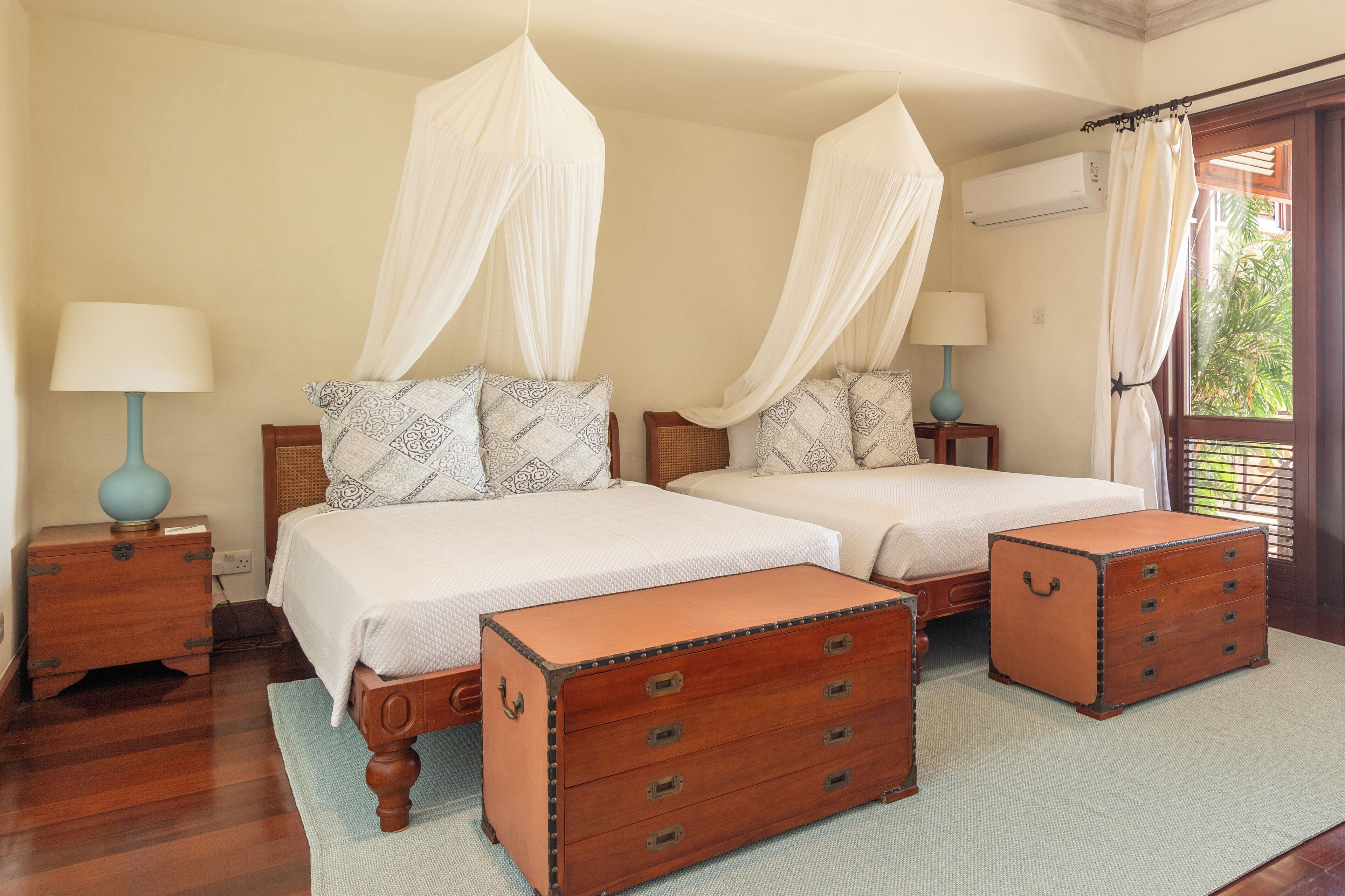 A double bed with a canopy, a wooden chest of drawers, and a bedside table with a lamp.