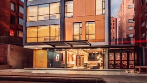 A modern multi-story hotel with a glass facade, a flat roof, and a ground-level entrance with a reception area. - Apartamentos Facile (Bogotá)