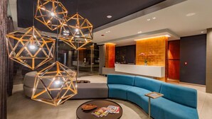 A modern lobby with geometric pendant lighting, a blue sofa, and a reception desk. - Apartamentos Facile (Bogotá)
