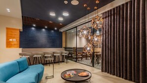 A modern lounge area with a blue sofa, a round coffee table, and a glass partition with a dining area in the background. - Apartamentos Facile (Bogotá)
