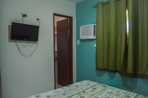 A bedroom with a bed, a television mounted on the wall, and an air conditioning unit.