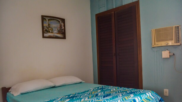 A bedroom with a bed, a wardrobe, a wall-mounted heater, and a painting. - Apartamento Mobiliado Mozart, 105 (Natal)