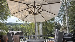 Un patio con una mesa redonda y sillas, una sombrilla y vistas a zona boscosa.