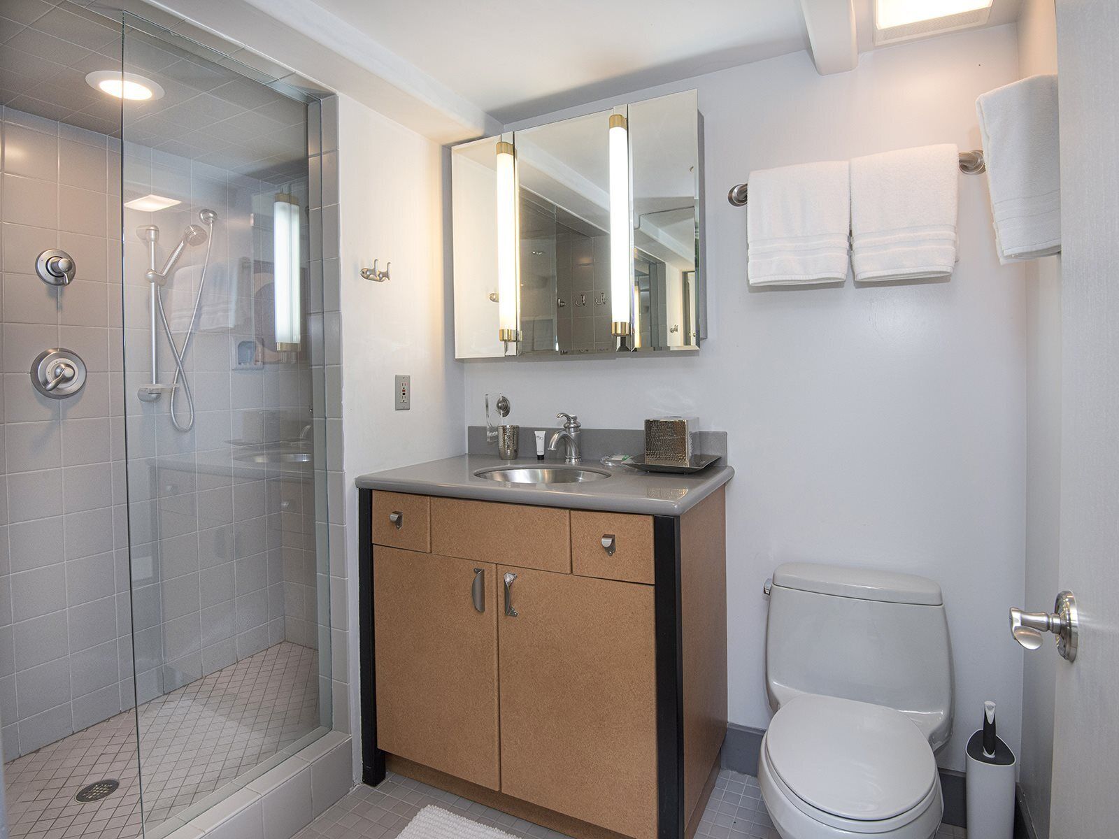Un baño moderno con ducha de vidrio, un lavamanos con espejo y un inodoro.