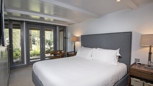 Un dormitorio moderno con una cama grande, una mesita de noche, una lámpara y un ventanal corredero que da a un balcón.