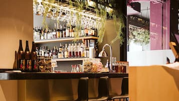 Una zona de bar con mostrador, taburetes y estanterías llenas de botellas y vasos.