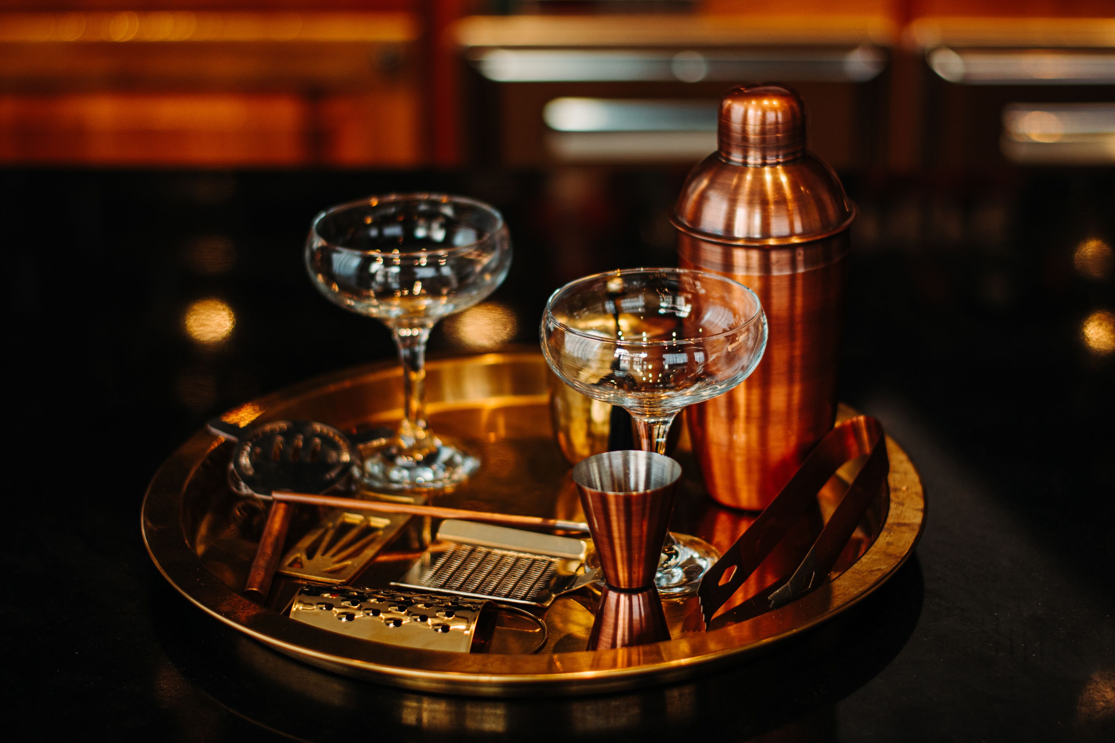 A cocktail tray with two glasses, a shaker, a jigger, and a bottle.