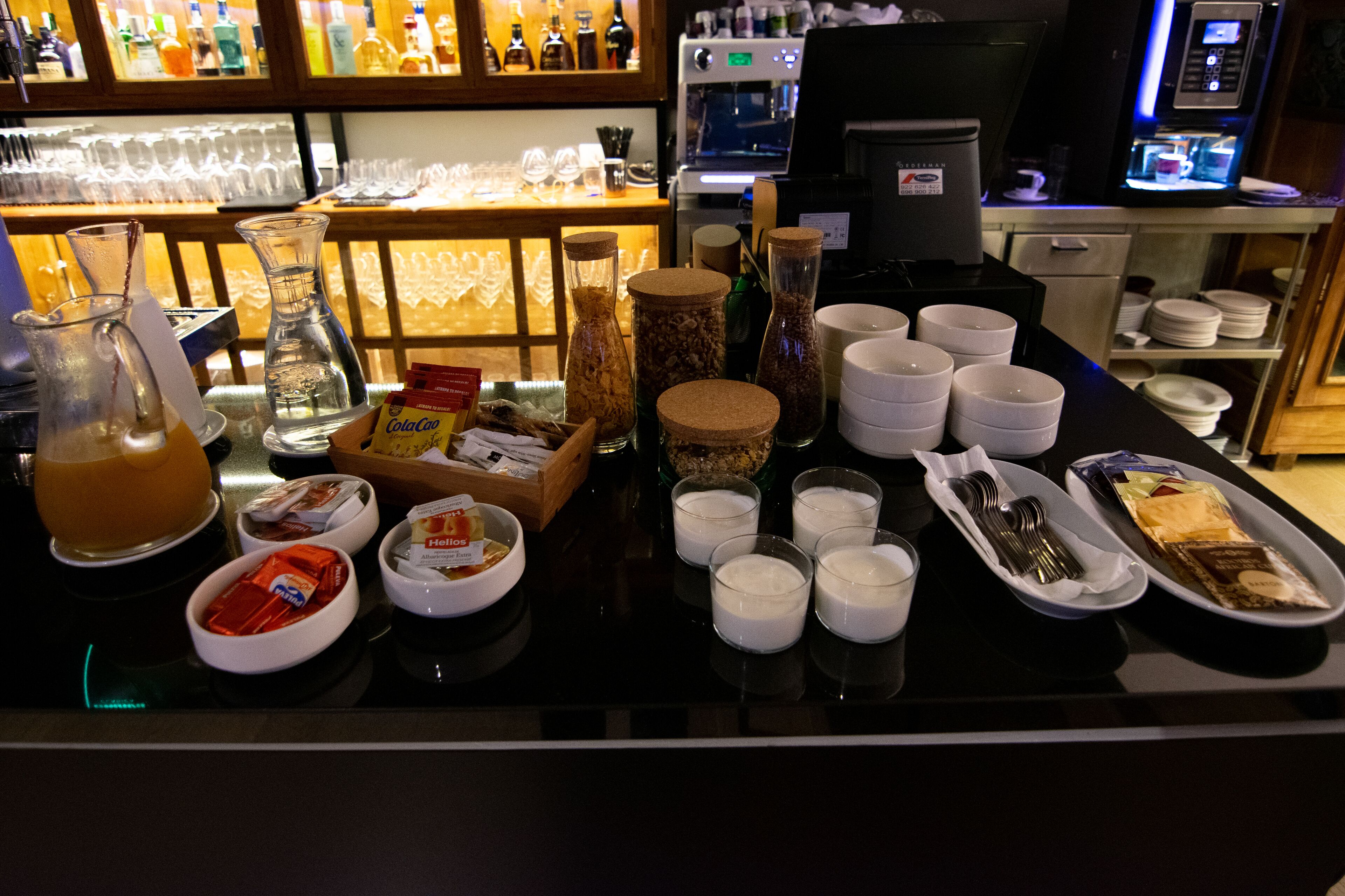 Zona de buffet per a l'esmorzar amb diferents aliments, salses i una màquina de cafè.