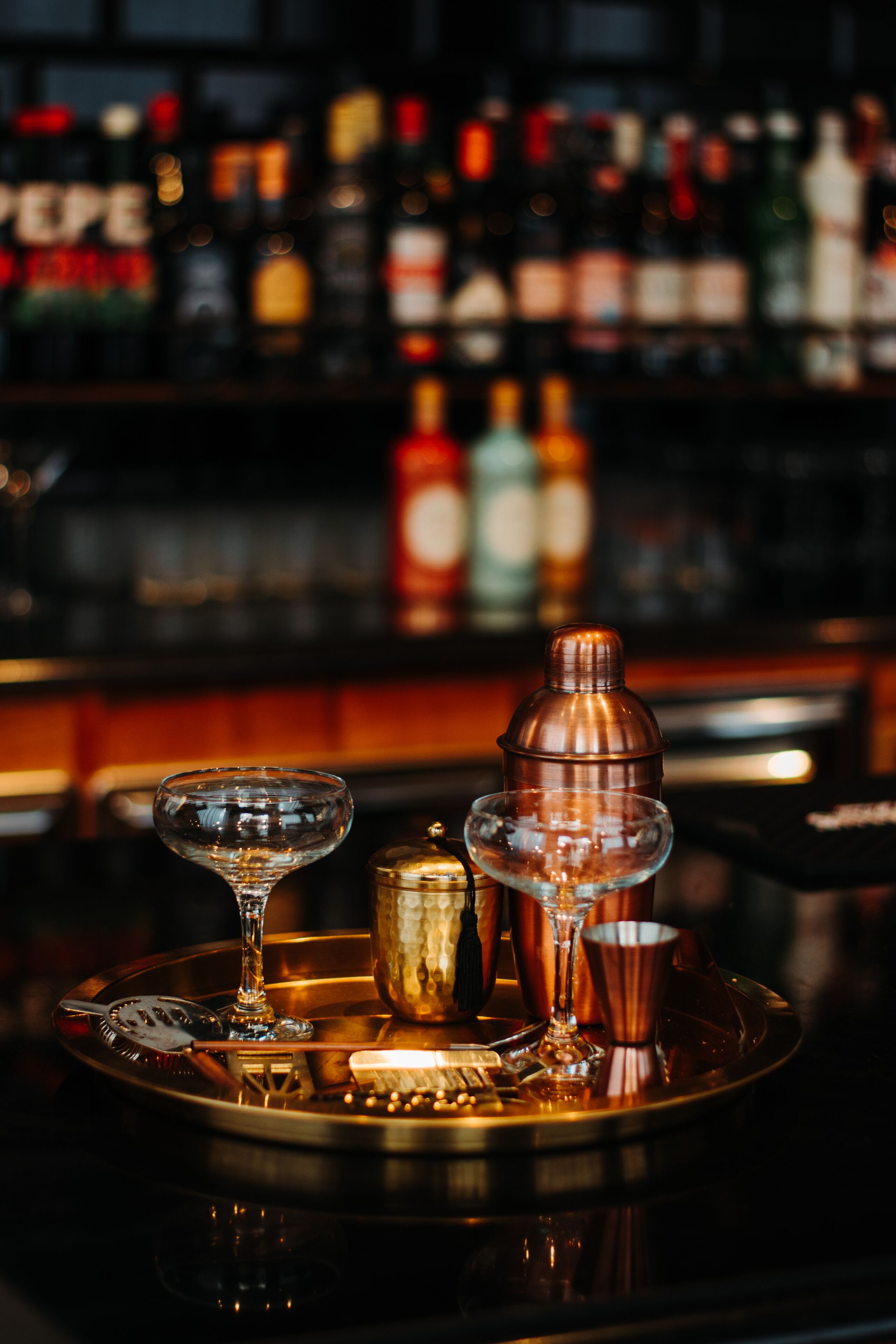 Een barsetting met een dienblad waarop een glas, een koperen cocktailshaker en een fles staan.