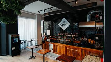 A bar area with a black brick wall, wooden bar counter, and stools. There is a vending machine and a menu board on the wall.