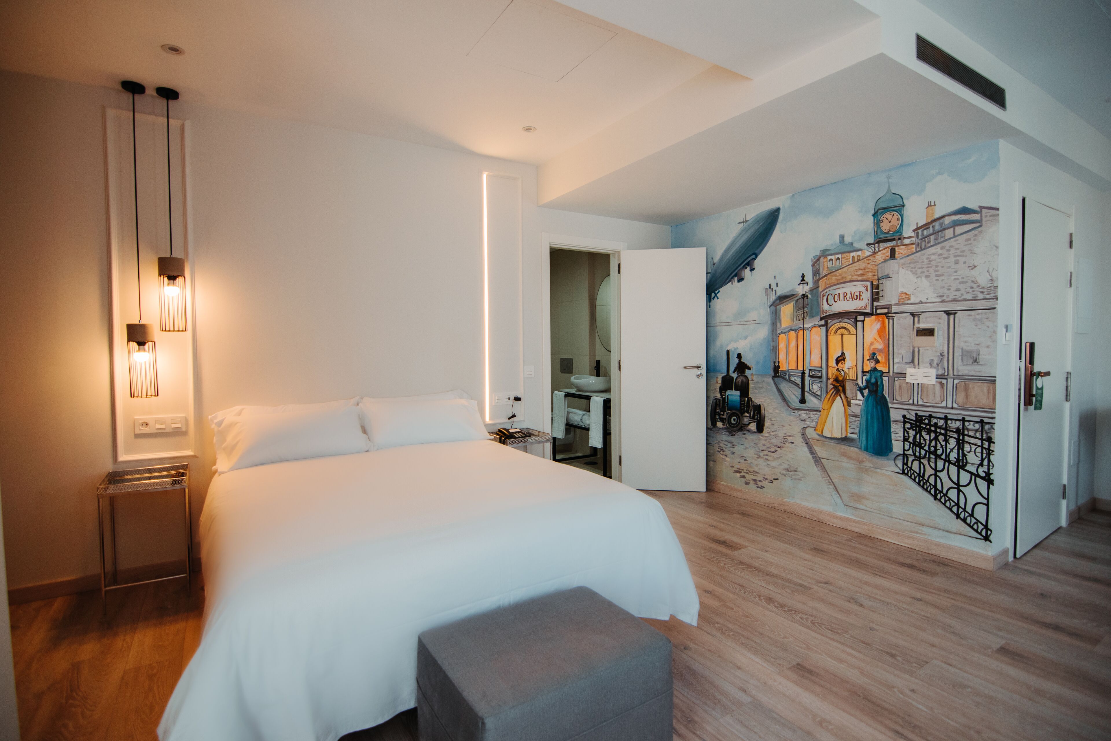 Habitación de hotel con una cama grande, una mesita de noche, un mural en la pared y un baño visible a través de una puerta abierta.