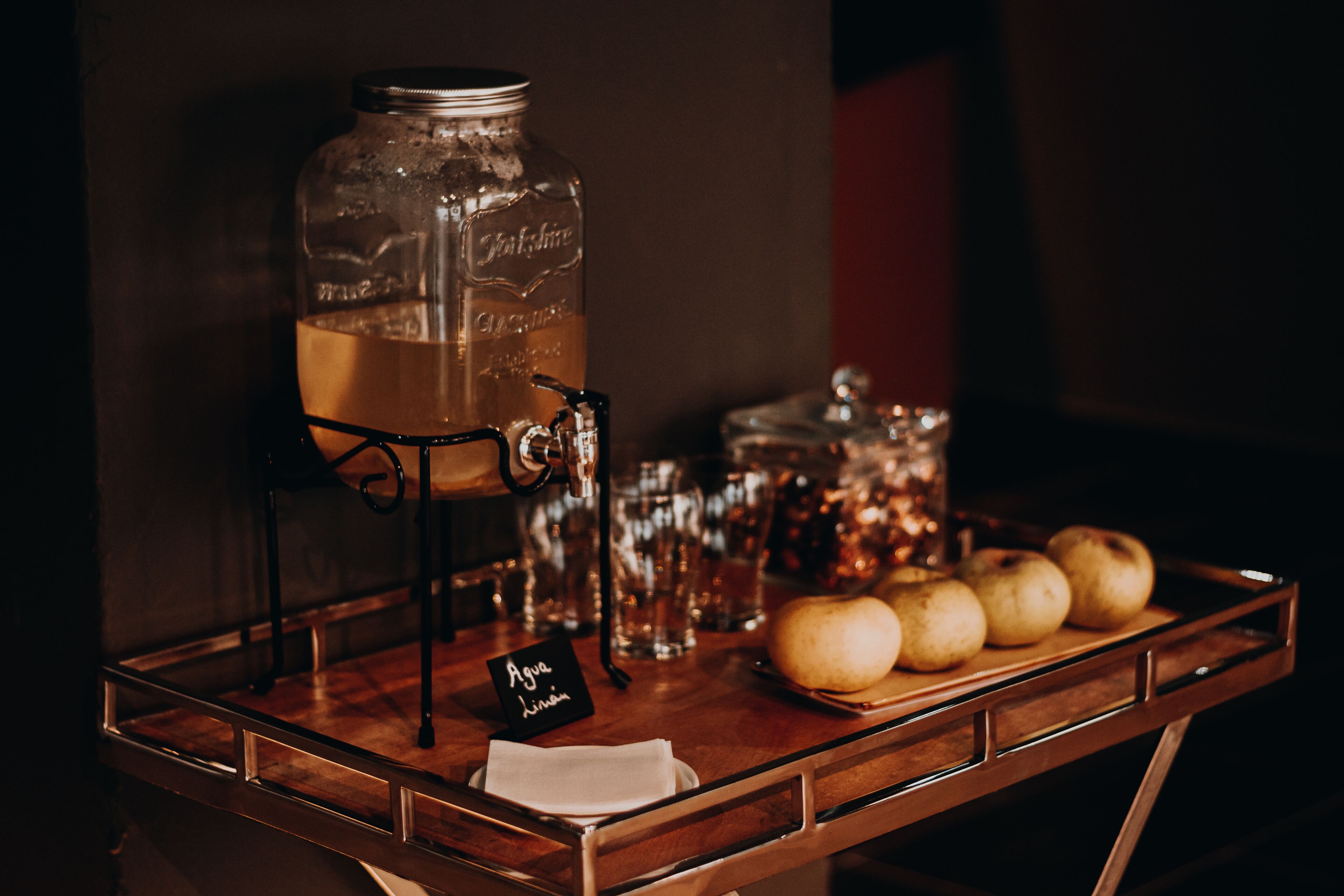 A bar area with a large glass jar, a metal stand, and a tray with apples.