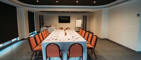 Sala de conferências com uma mesa comprida, cadeiras laranja e um quadro branco.