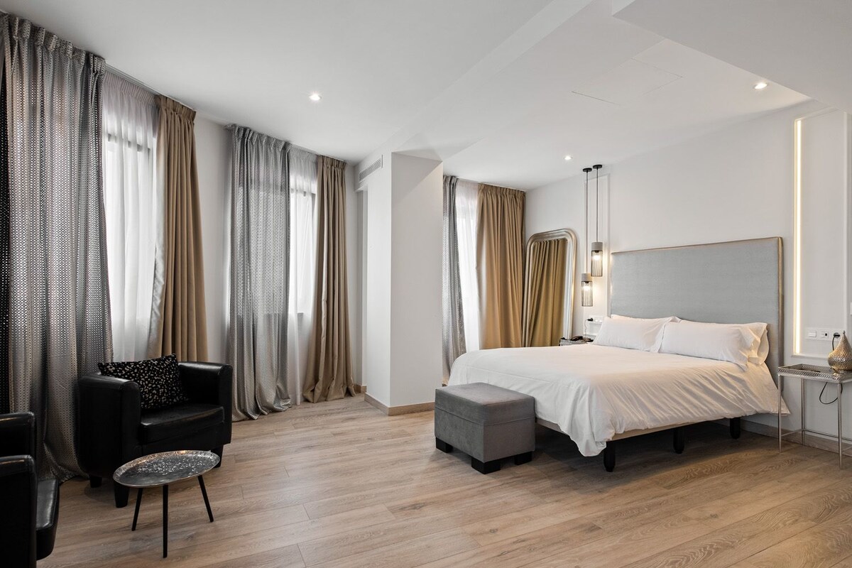 Habitació d'hotel moderna amb un llit gran, una taula de nit, una cadira i una taula petita.