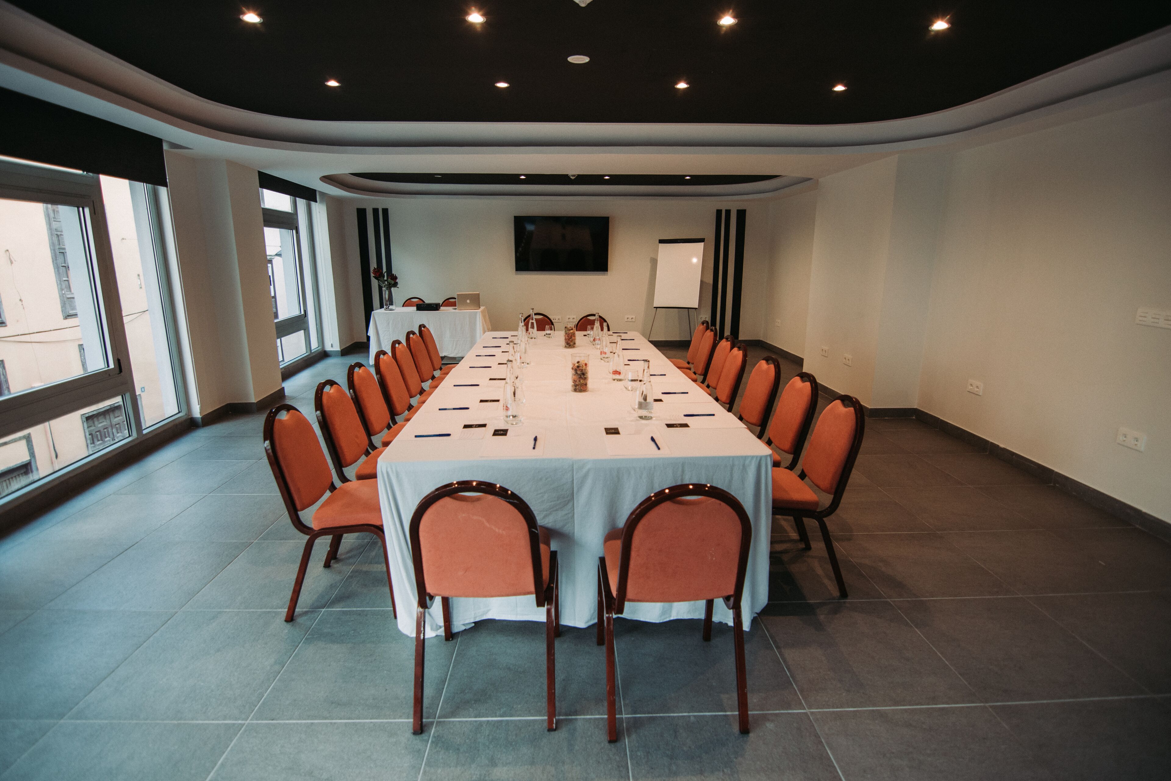 Ein Konferenzraum mit einem langen Tisch, orangefarbenen Stühlen und einer Whiteboard-Tafel.