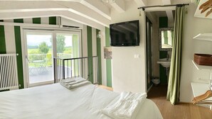 Un dormitorio con cama, televisor, baño y balcón con vistas.
