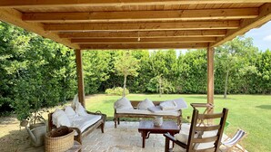 Un patio al aire libre con mobiliario de madera, suelo de piedra y una pérgola.