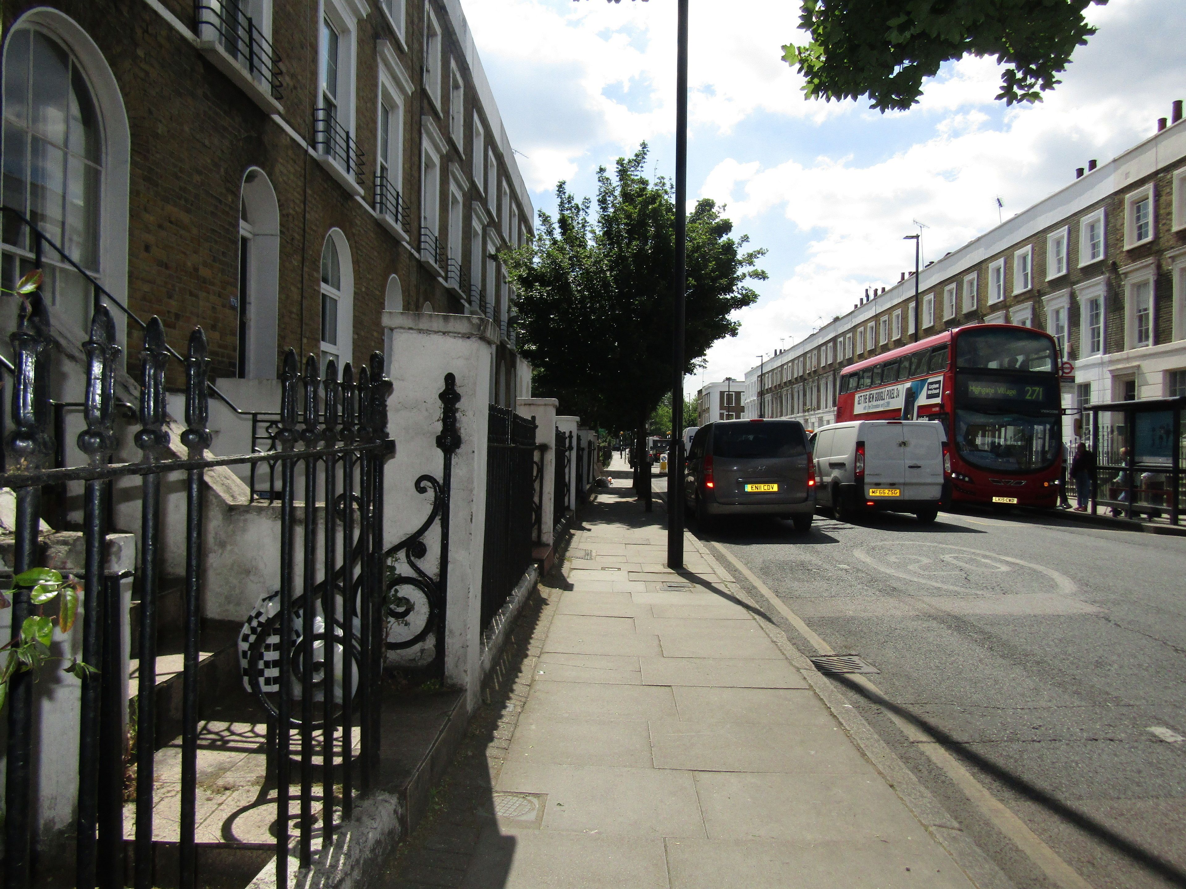 A street with a double-decker bus, parked cars, and a sidewalk.