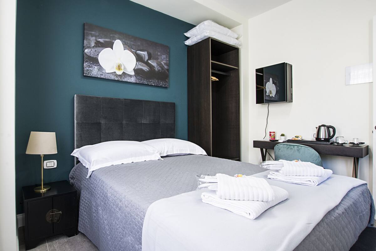 A hotel room with a bed, a desk, a chair, a lamp, and a painting on the wall.
