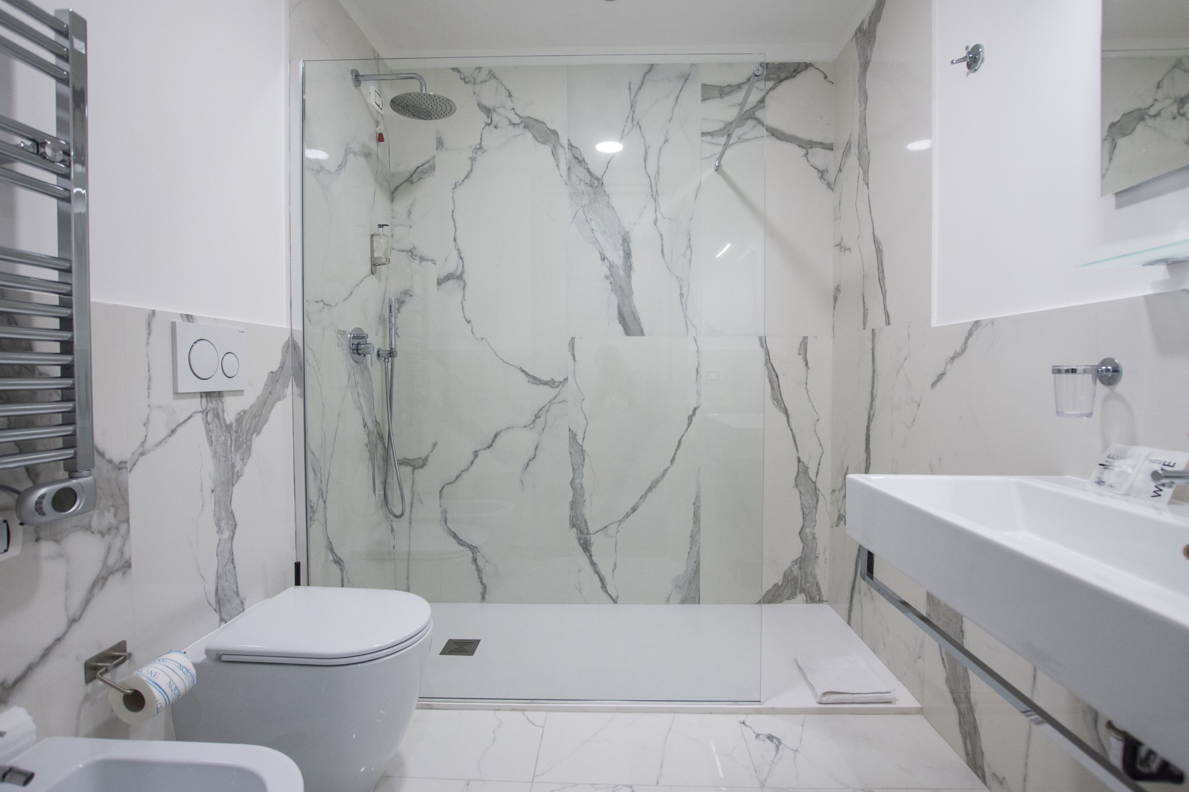 Un baño moderno con ducha de vidrio, inodoro blanco y lavamanos con espejo.