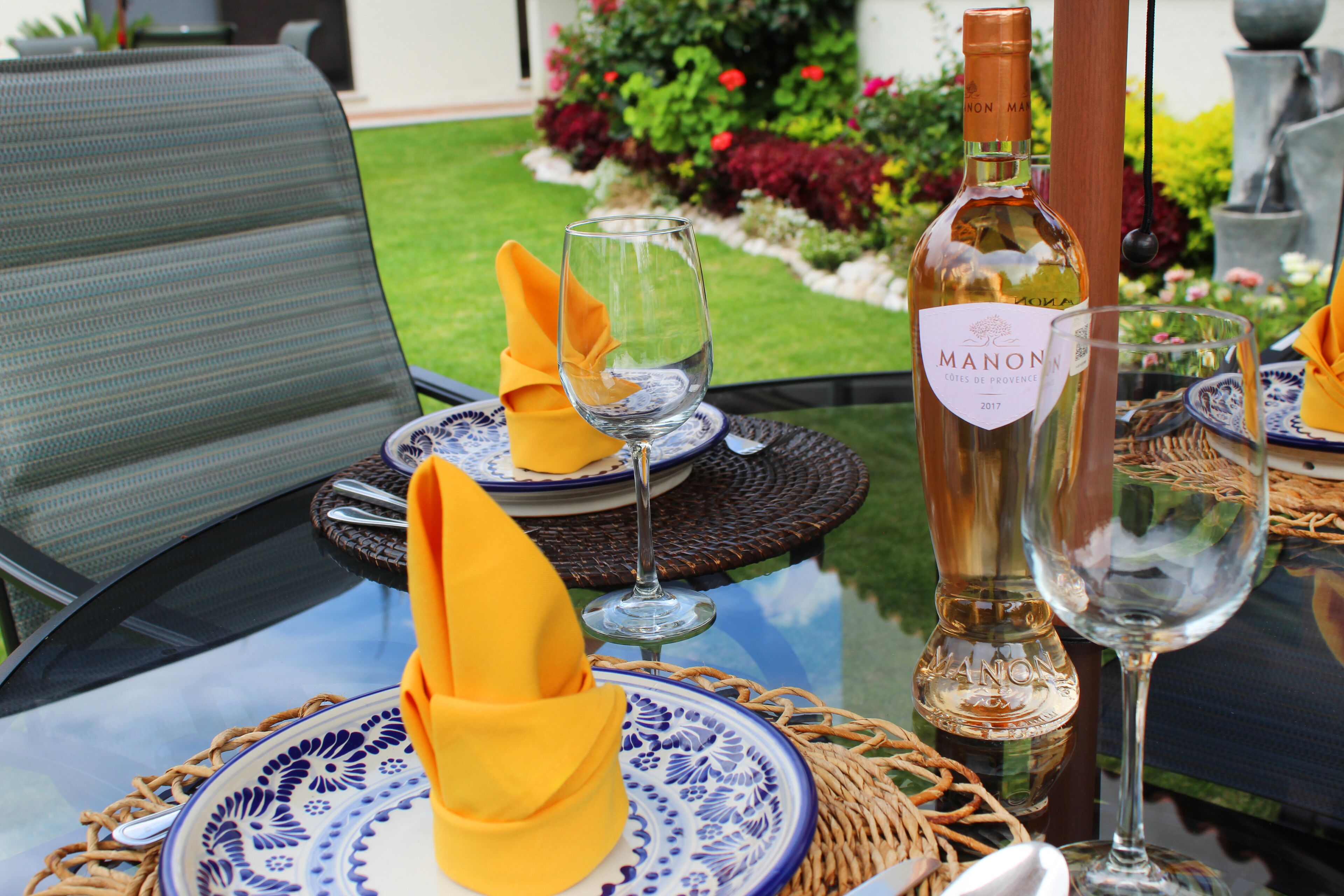 Ein Tisch ist mit blau-weißen Tellern, gelben Servietten und einer Flasche Manon Wein gedeckt.