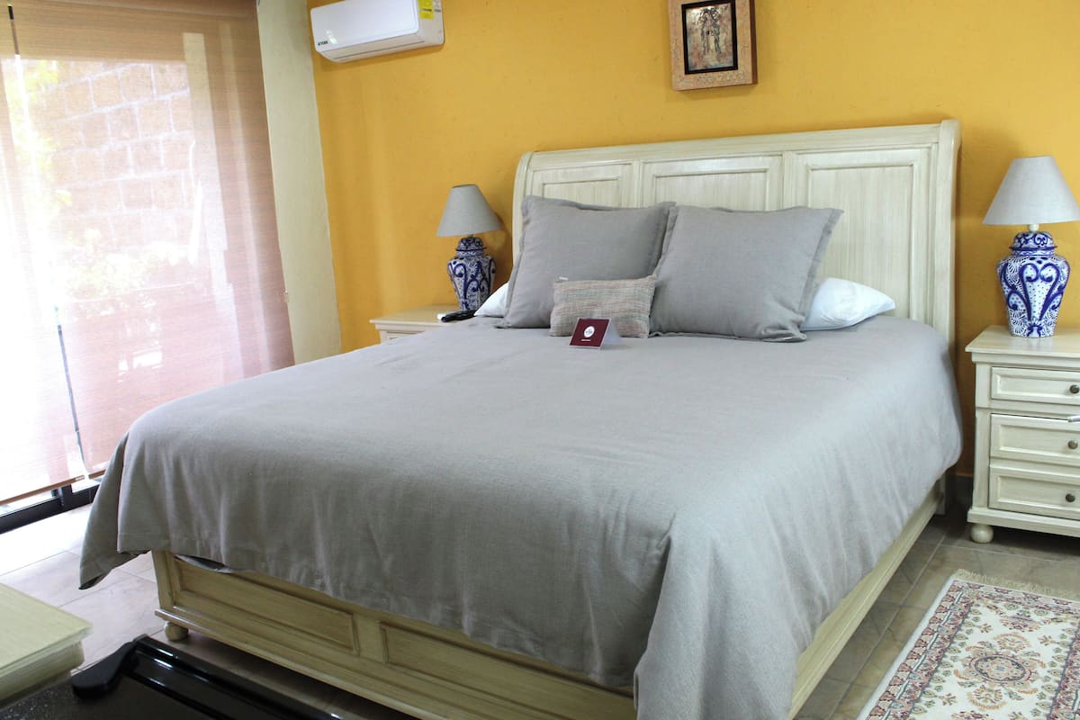 A neatly made bed with a grey bedspread and pillows, two bedside tables with lamps, a small rug, and a picture on the wall.