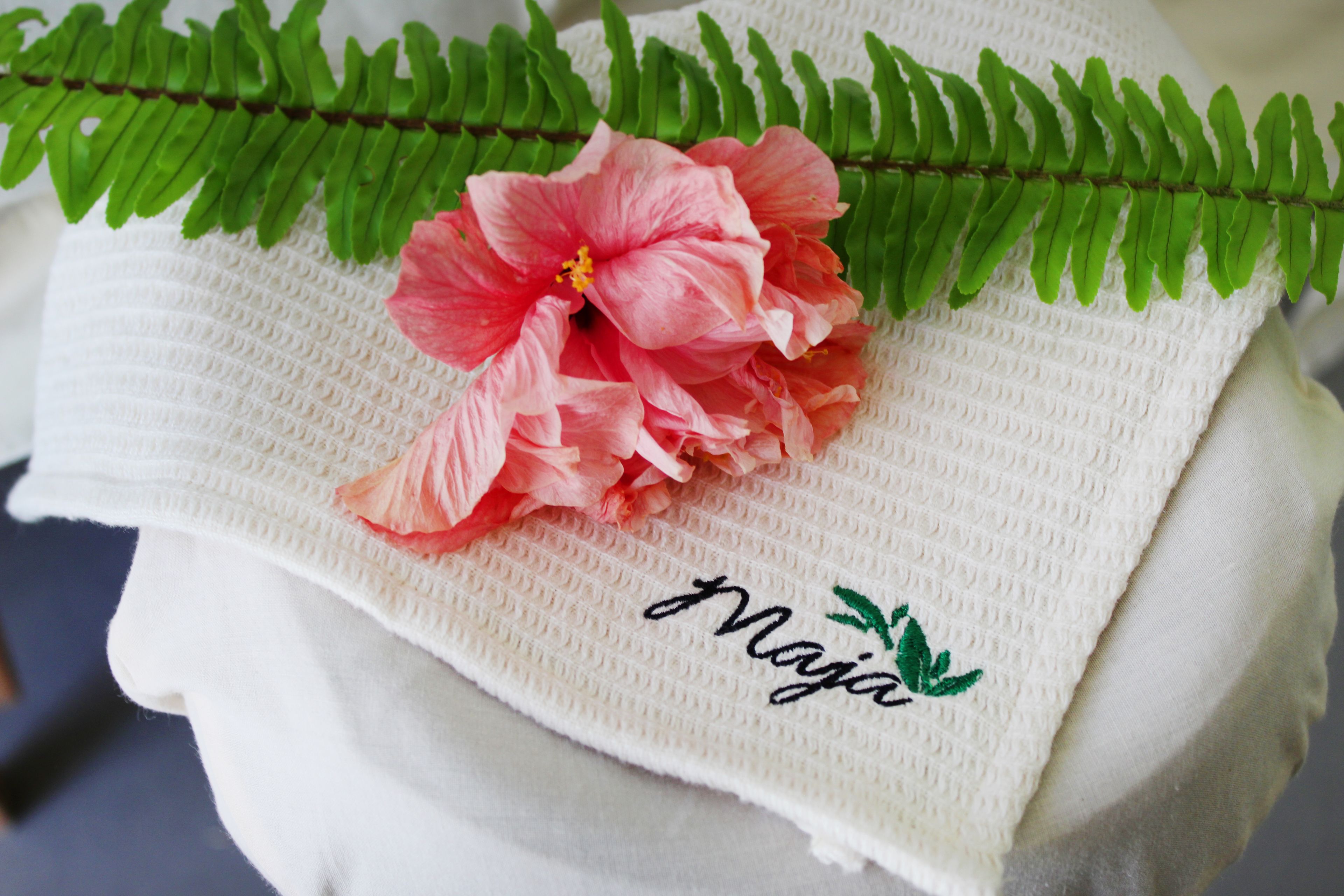 A white towel with a pink hibiscus flower and a fern leaf.