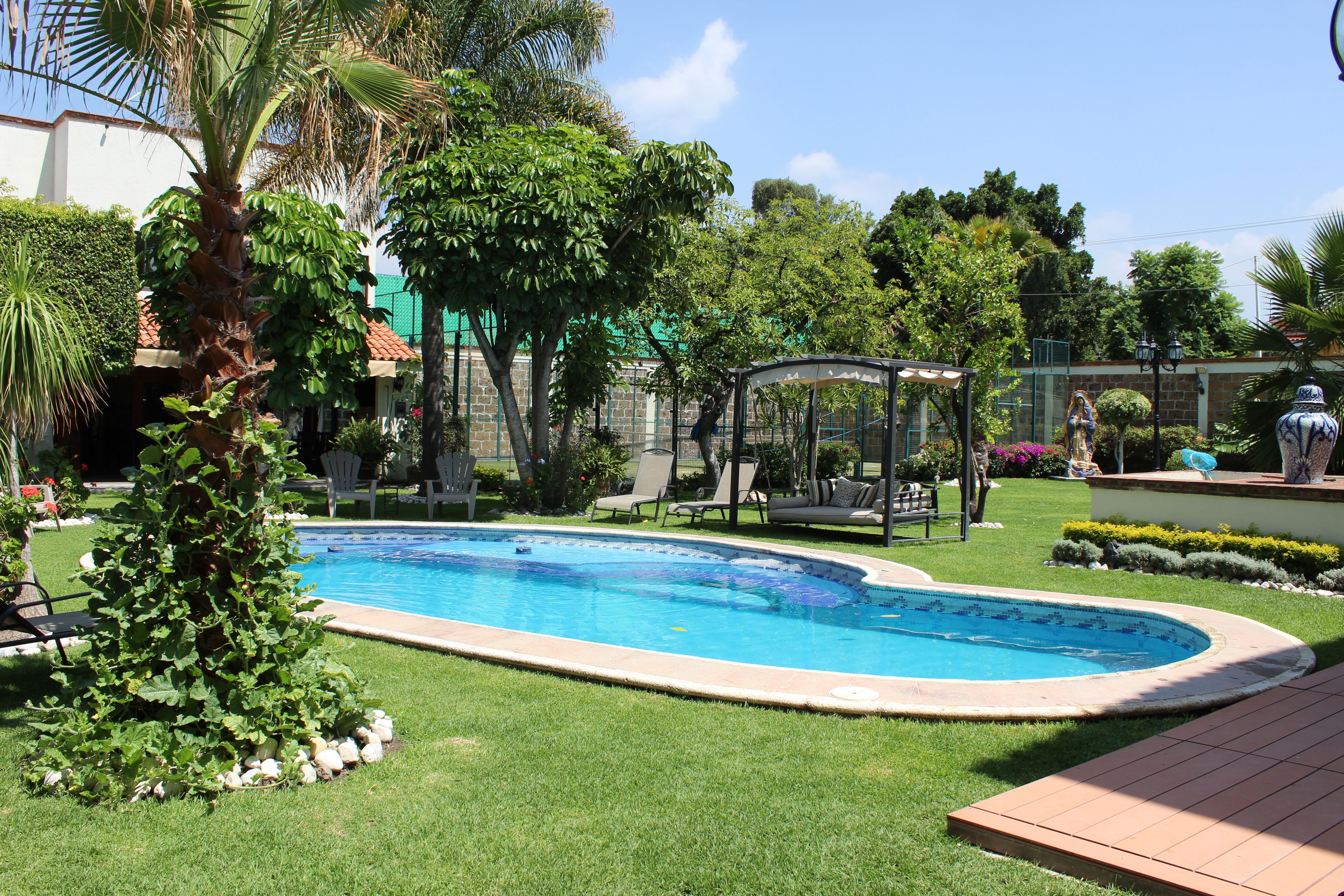 A swimming pool surrounded by a well-maintained lawn, a gazebo, and various plants.