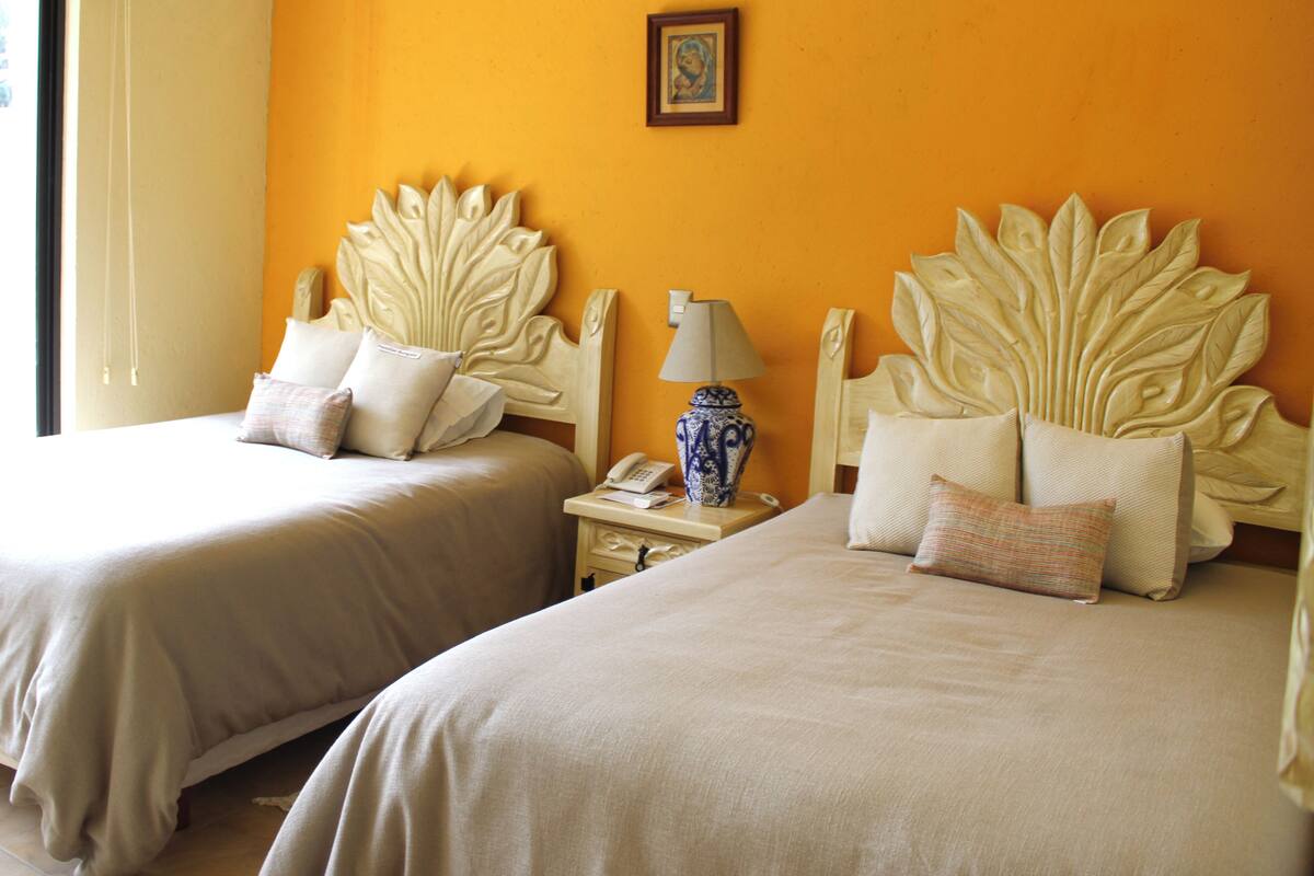 Two beds with leaf-shaped headboards, a bedside table with a lamp, and a framed picture on the wall.