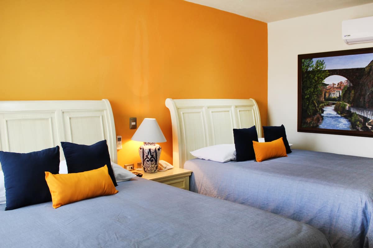 A hotel room with two beds, each with matching pillows and a nightstand with a lamp.