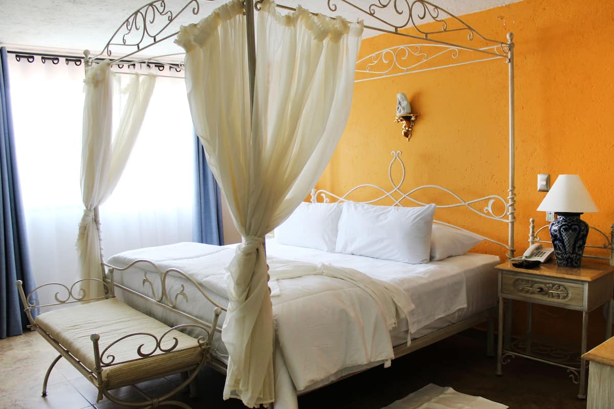 A four-poster bed with white linens, a bedside table with a lamp, and a wall-mounted telephone.