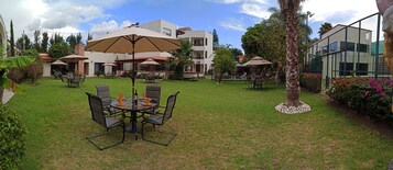 Un patio con mobiliario exterior, palmeras y un edificio con techo de tejas.