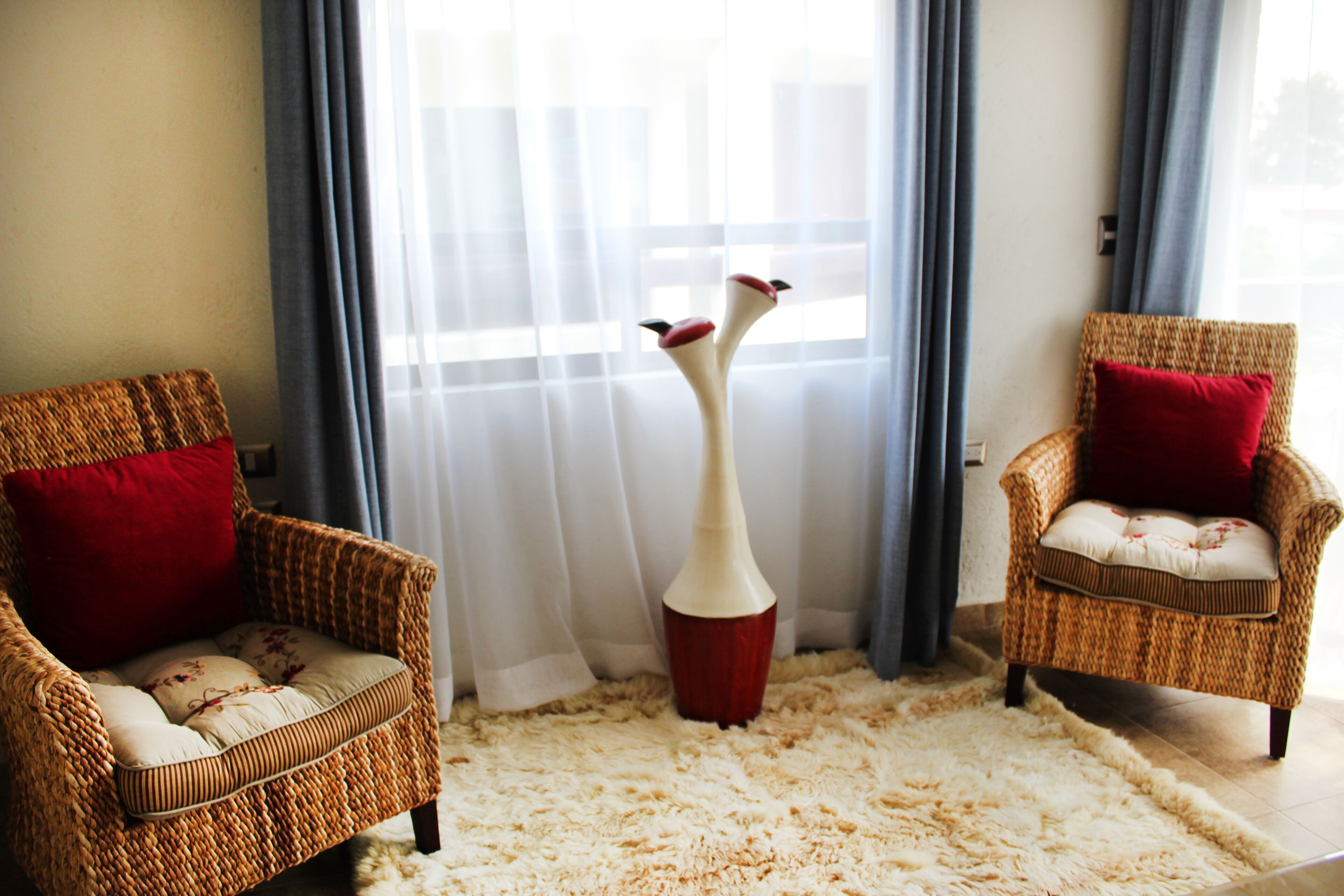 A room with two wicker chairs, a fluffy rug, and a tall vase.