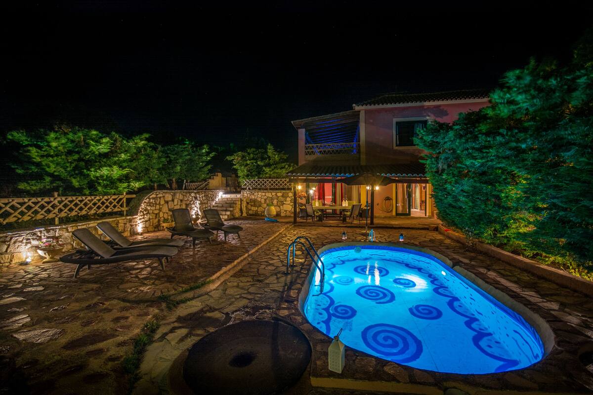 A nighttime outdoor pool area with lounge chairs and a hot tub.