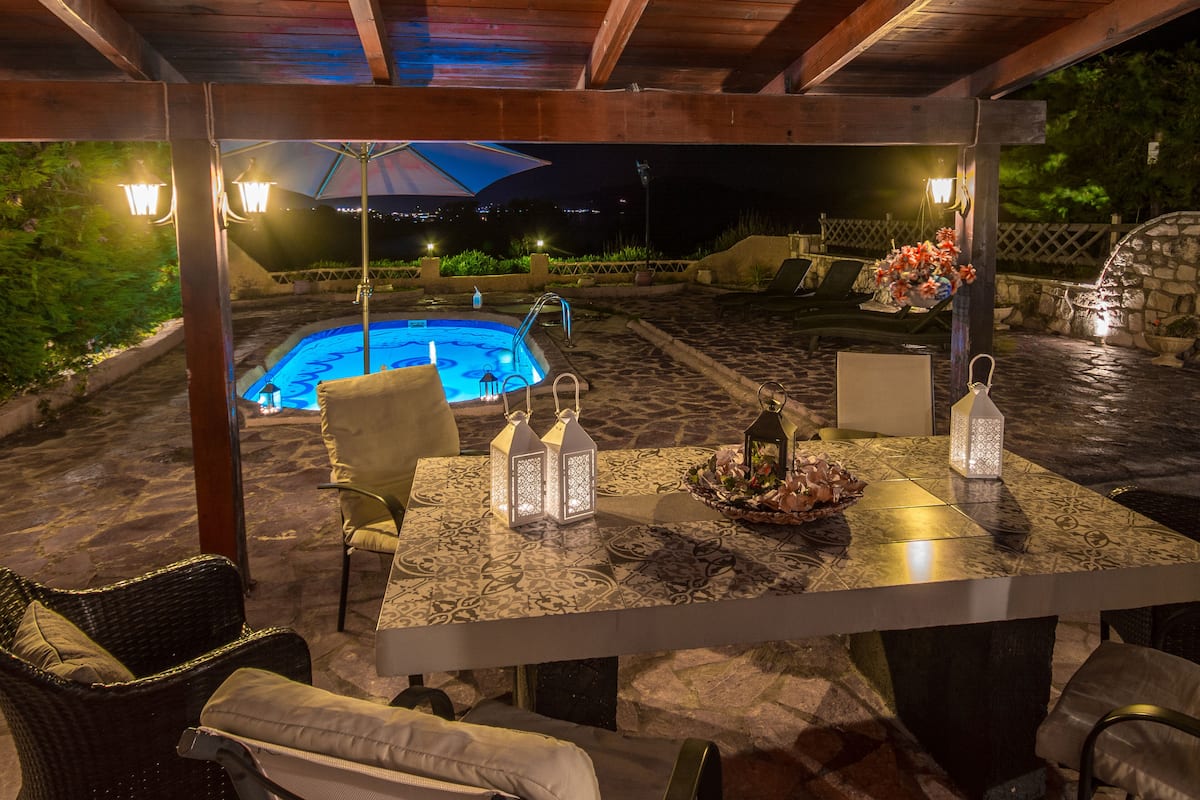 An outdoor pool area with a covered patio, lounge chairs, and a table set for dining.