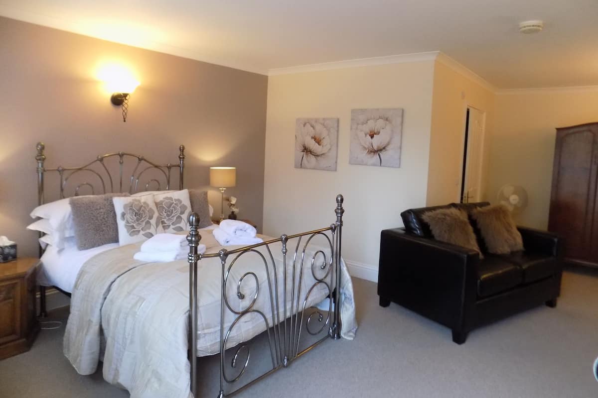 A bedroom with a bed, bedside tables, a black leather sofa, and two wall-mounted lamps.
