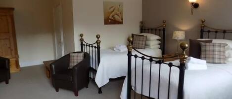 A bedroom with two beds, a wooden wardrobe, a chair, and a painting on the wall.