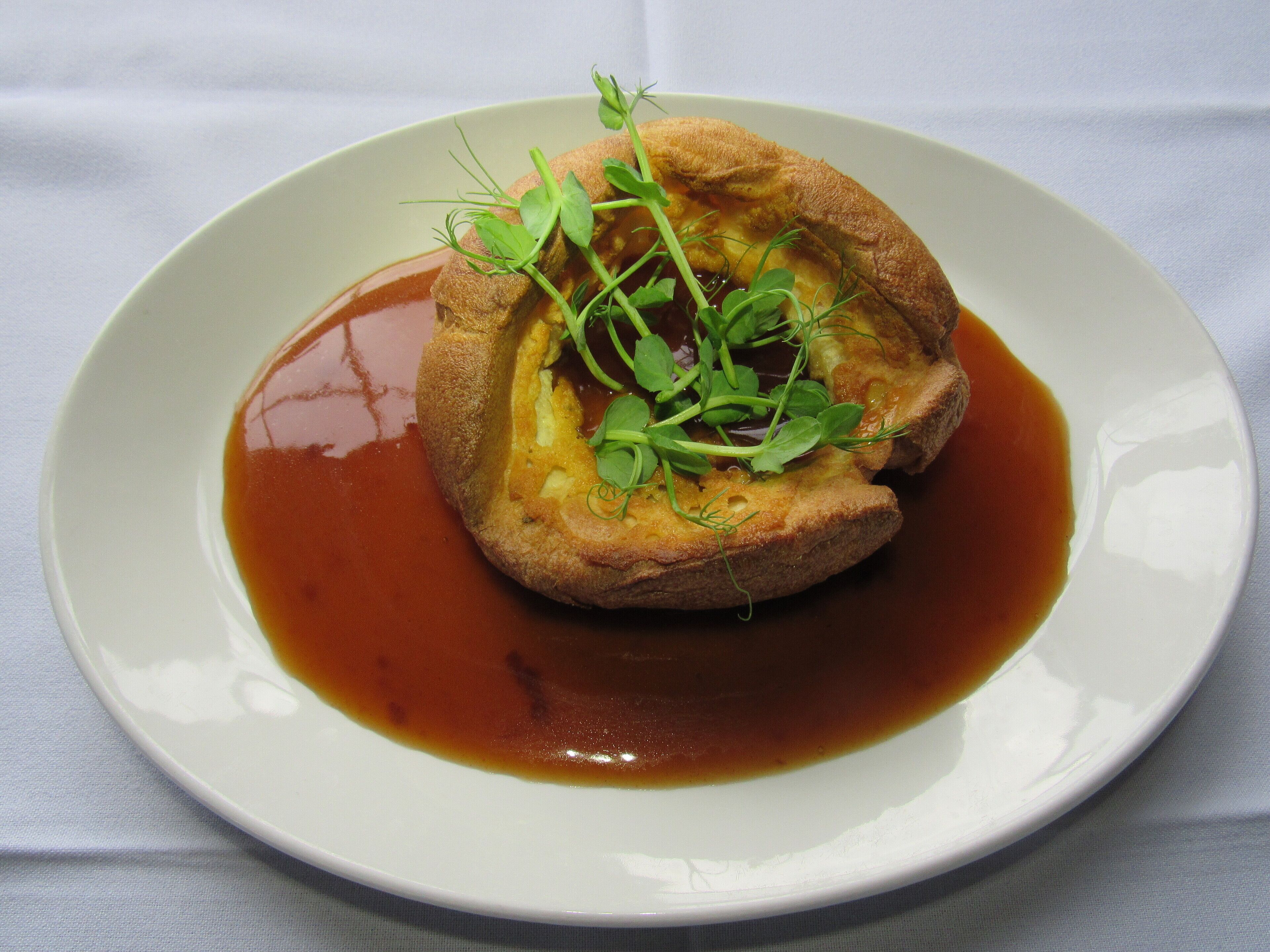 A plate with a Yorkshire pudding, gravy, and greens.