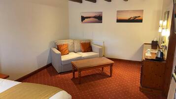 A cozy room with a sofa, a wooden coffee table, a bed, and a small cabinet with a kettle.