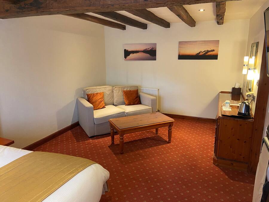 A cozy room with a sofa, a wooden coffee table, a bed, and a small cabinet with a kettle.